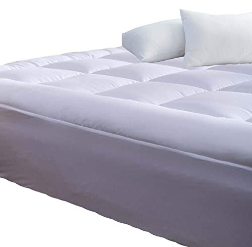 White bed with pillows, featuring a thick mattress topper.